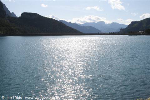 Alpine lake with dam, sunlight sparkling on the water among mountains