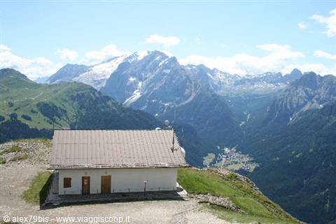 Mountain hut with metal roof on alpine meadow, snowy dolomite peaks above green valley
