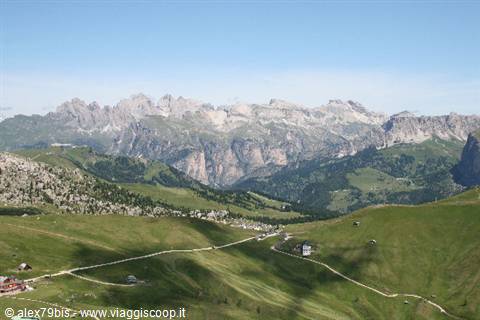 Green slopes and rocky Dolomite peaks, cable car shadow crossing the hillside