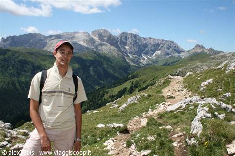 Hiker with backpack on rocky grassy trail, Dolomites peaks in background