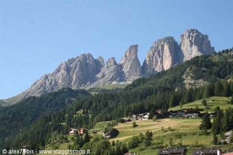Sassolungo group above a village with green meadows and firs