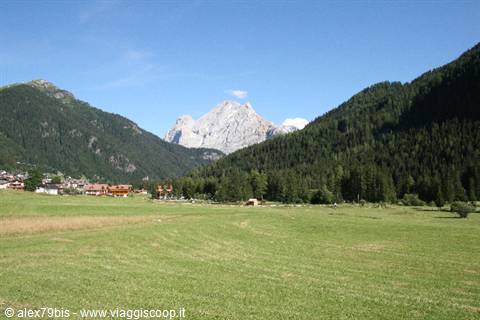 wooden village at the foot of the Dolomites, green meadow under blue sky