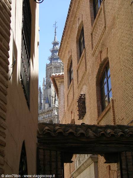 Toledo Cathedral spire rising between brick buildings under bright sun