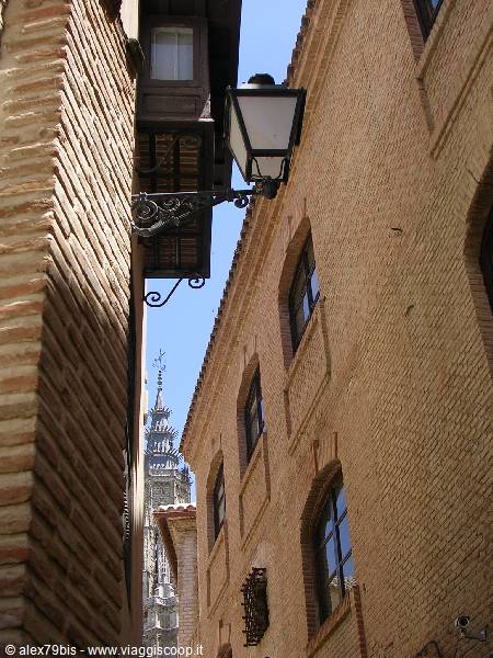 Iron lantern between brick walls, Toledo cathedral tower in the background