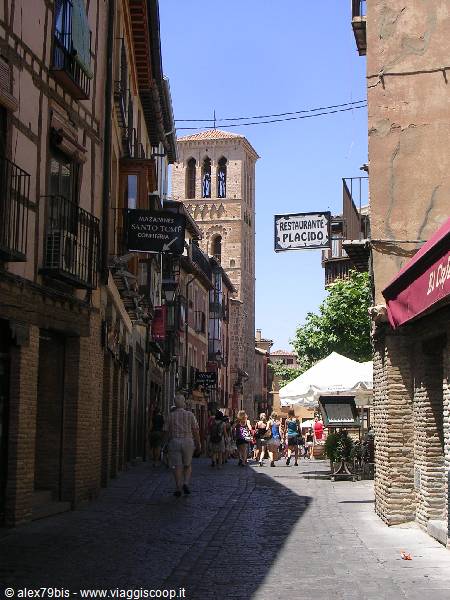 Tourists walk past half-timbered houses toward the Romanesque tower of Santo Tomé church in Toledo