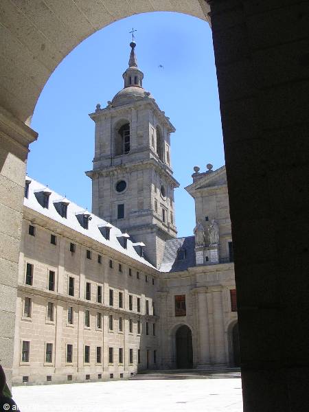 The bell tower of El Escorial framed by a stone arch, blue sky