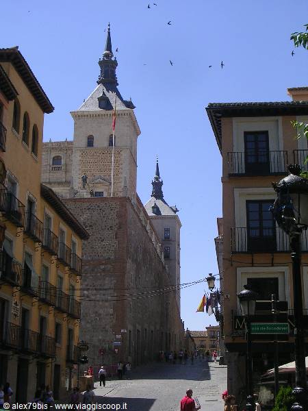 The Alcázar of Toledo above the street, brick buildings, flags, tourists walking