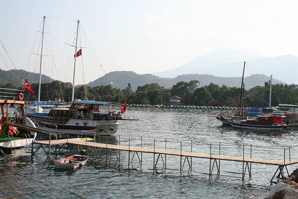 Turkish wooden gulets moored at a metal pier, hazy mountains behind