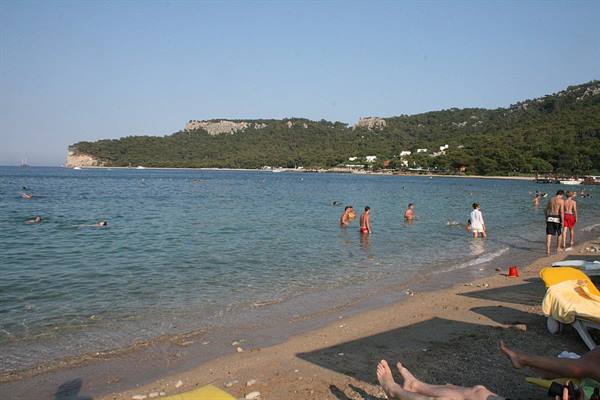 Tourists swimming at a sandy beach with green rocky hills behind