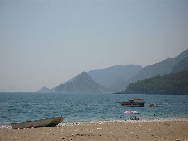 White boat on sandy beach, pedal boat and hazy blue mountains by calm sea