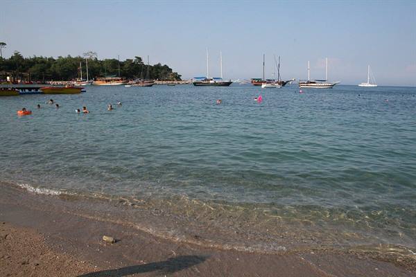 Swimmers in turquoise water near sailboats, sandy beach in daylight