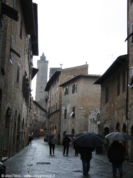 Rain in San Gimignano: people with umbrellas among medieval stone towers