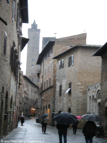 People with umbrellas in the rain on medieval street, San Gimignano tower