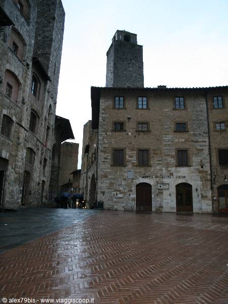 Medieval stone tower above San Gimignano houses, wet pavement after rain