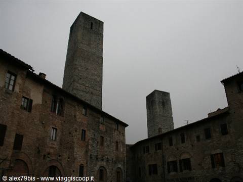 Medieval towers of San Gimignano rising above stone houses under a gray sky