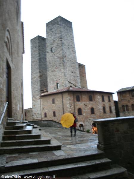 Tourist with yellow umbrella beneath the medieval towers of San Gimignano