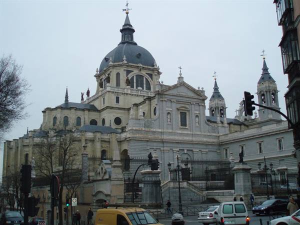 Almudena Cathedral with dark dome, street traffic and traffic lights under grey sky