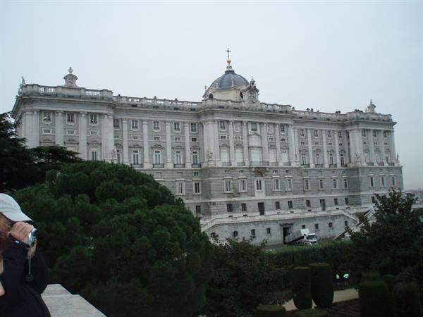 Royal Palace of Madrid in pale stone, dome with cross, tourist photographing among trees
