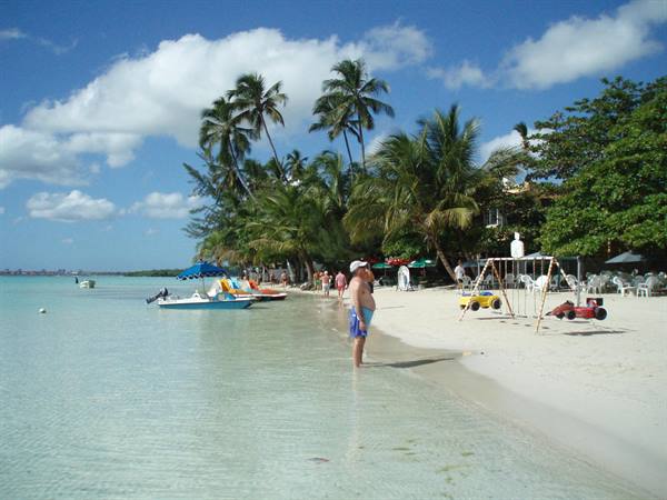 Barefoot tourist in shallow water, palm-lined beach with small colorful boats