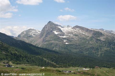 Rocky snowy peaks above a green alpine valley with huts