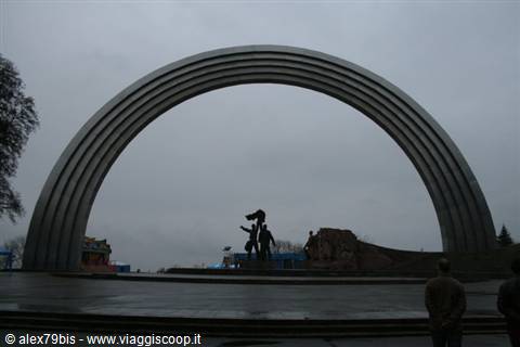 Steel friendship arch in Kyiv with statue beneath a grey sky