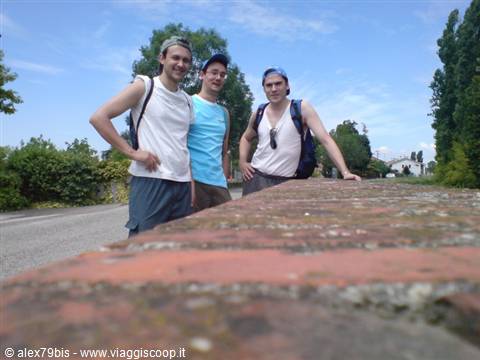 Three backpackers leaning on a brick wall along a sunny country road