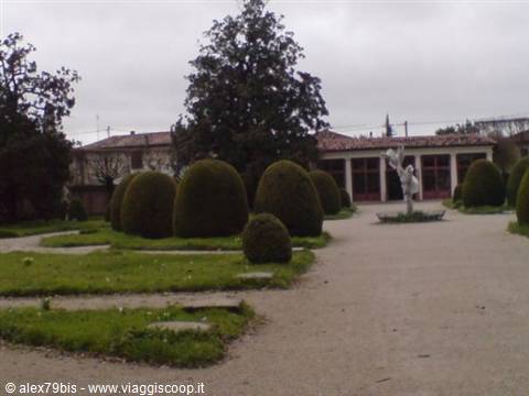 Statue on pedestal in a garden with rounded hedges under grey sky