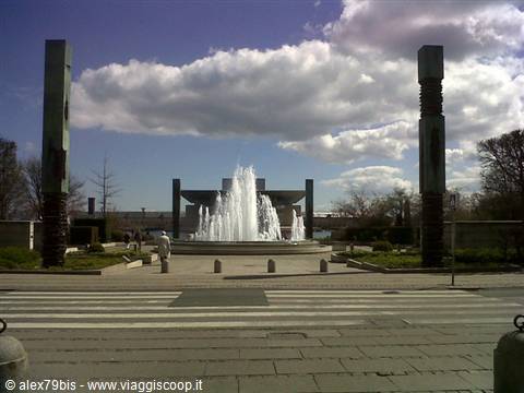 Fountain spraying water in paved square between stone pillars and clouds