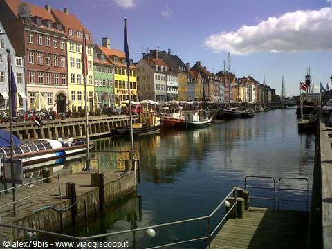 Colorful townhouses along Nyhavn canal in Copenhagen, boats moored under sunny sky