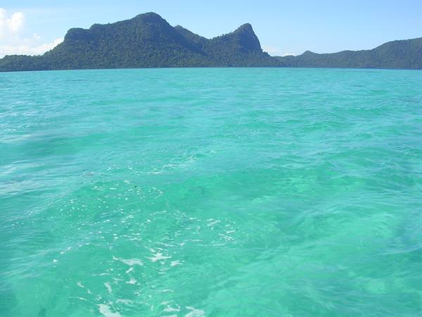 Clear turquoise water in front of green mountainous islets under blue sky