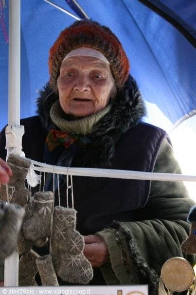 Elderly woman in wool hat sells felt booties under the blue umbrella