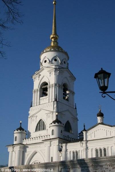 White bell tower with golden spire and wrought-iron lantern, blue sky