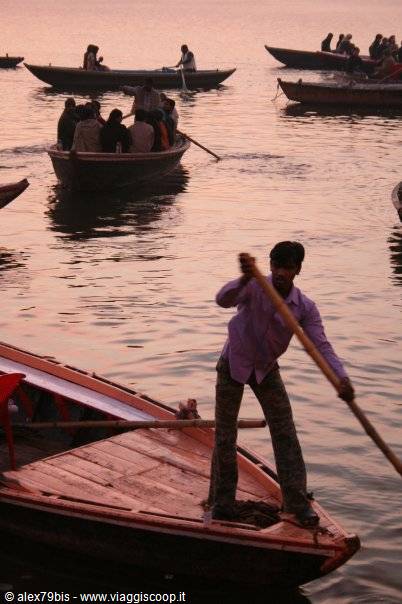 Boatman rows standing on the Ganges river in Varanasi, wooden boats at dusk