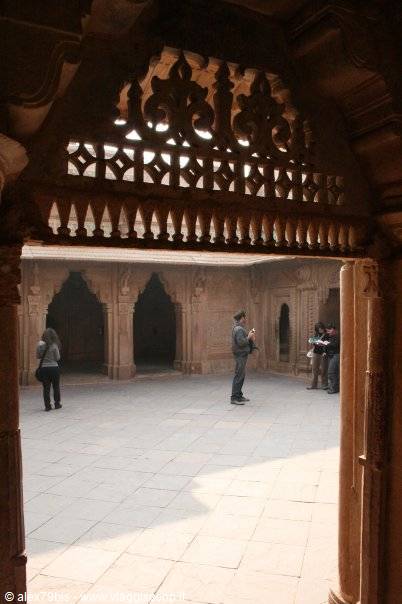 Tourists in a sandstone courtyard of a palace with carved arches