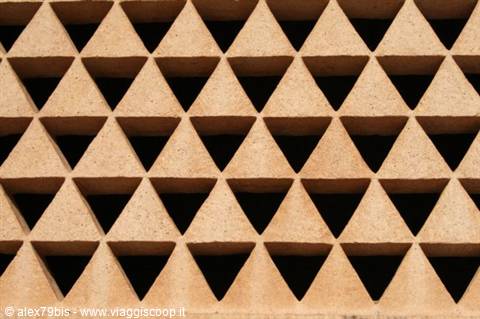 Sandstone perforated wall with repeating hollow triangles under direct sunlight