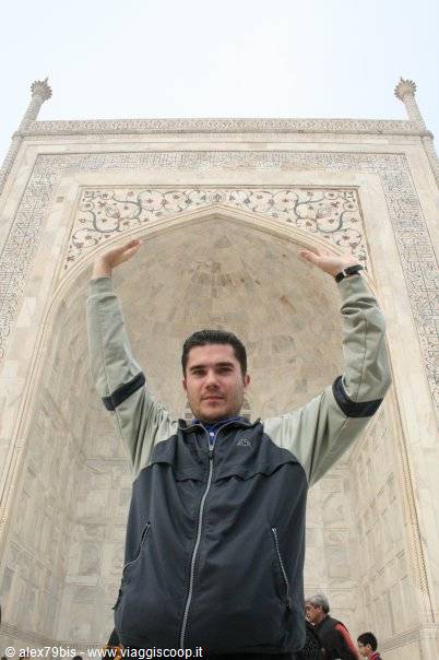 Tourist posing with raised arms under the Taj Mahal's carved marble arch