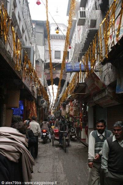 Crowded narrow bazaar lane with golden tinsel decorations, cyclist and pedestrians