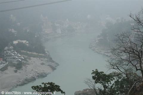 The Ganges shrouded in fog at Rishikesh, buildings and trees line the riverbanks