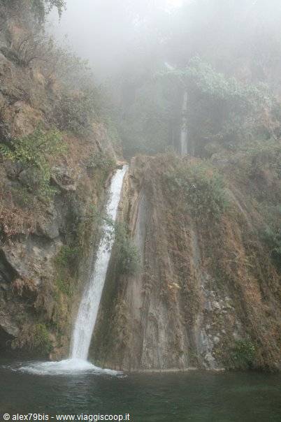 Waterfall cascading over mossy rock in fog, green pool below