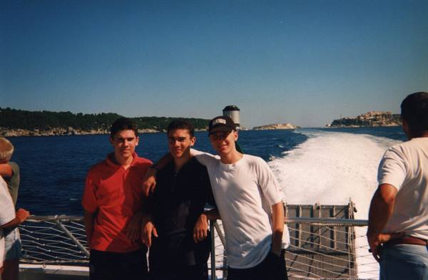 Three boys posing on a ferry stern deck, white wake behind