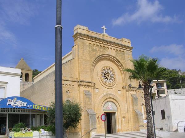 Yellow stone church facade in Lampedusa with rose window and palm
