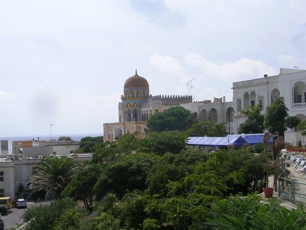Brick dome above white buildings among greenery, cloudy sky, distant sea