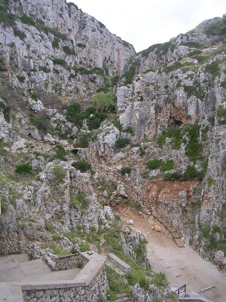 Wooden staircase winding between limestone cliffs and Mediterranean shrubs at Capo Caccia