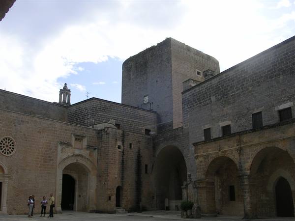 Stone castle courtyard with massive tower, arches, cloudy sky and few visitors