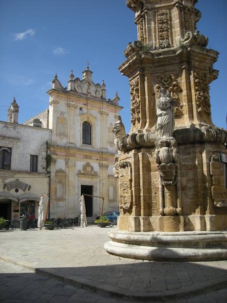 Baroque stone column in front of Nardò church under midday sun