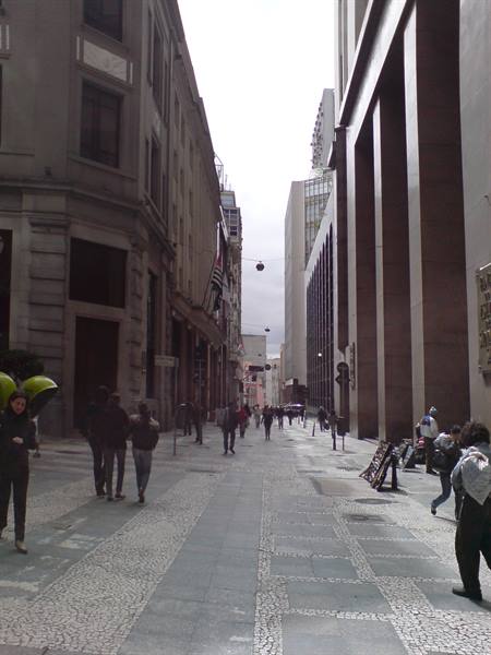 Pedestrians walk on Portuguese mosaic street between tall buildings under cloudy sky