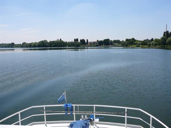 Boat bow with blue flag sailing on a lake with tree-lined shores
