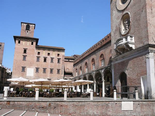 Mantua, Piazza delle Erbe: clock tower and outdoor café with white umbrellas under blue sky