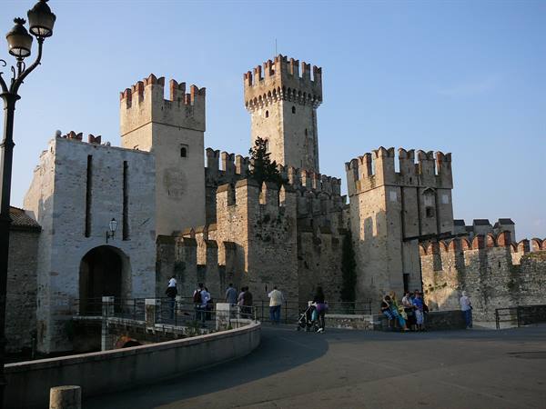 Tourists before Sirmione's Scaliger castle, crenellated stone walls in evening light