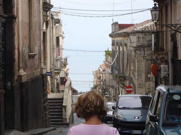 Girl in pink walking down a stone street with parked cars and sea ahead